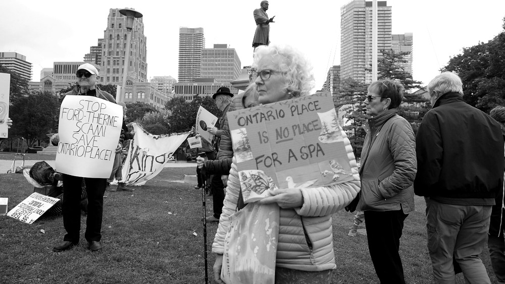 Queens Park rally crowd for Ontario Place a woman holds a sign, that says Ontario Place is no place for a spa